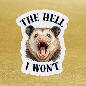 May include: A sticker with an illustration of an opossum with an open mouth. The text "THE HELL I WON'T" is above and below the opossum. The sticker has a white border and a gold background.