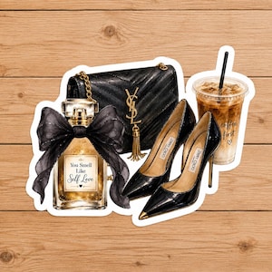 Peut inclure: Un sac à main noir matelassé avec un logo doré, un flacon de parfum en verre avec un nœud noir et le texte You Smell Like Self Love, des escarpins noirs à talons hauts avec des bouts dorés, et un gobelet de café glacé avec le texte coffee first.