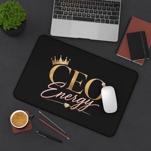 Op de afbeelding: Een rechthoekige zwarte muismat met de gouden tekst CEO en roze cursieve tekst Energy. Boven het woord CEO staat een gouden kroon en onder het woord Energy bevindt zich een klein gouden hartje. Het ontwerp staat centraal op het oppervlak.