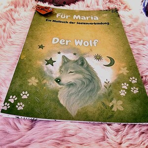 Könnte beinhalten: Ein Malbuch mit dem Titel "Der Wolf" mit einer Wolfsillustration. Das Cover zeigt einen Wolfskopf, Sterne, Blumen und Pfotenabdrücke auf einem grün-gelben Hintergrund. Das Buch ist Maria gewidmet.