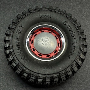 Puede incluir: Neumático negro con una llanta roja y cromada y un logotipo de Volkswagen gris. El neumático dice "Crawler Master" y "All Terrain M/T" en el lateral.