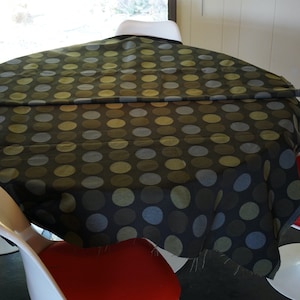 May include: A round table with a black tablecloth featuring a repeating pattern of green and blue polka dots. Four white chairs with red cushions surround the table.