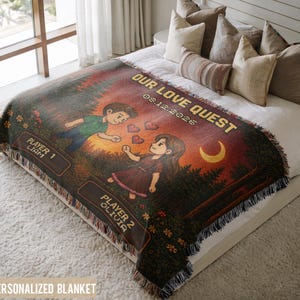 Peut inclure: Un plaid tissé présentant une scène artistique numérique avec deux personnages, un croissant de lune et des cœurs rouges. Le texte indique OUR LOVE QUEST, 08.12.2026, PLAYER 1 LIAM et PLAYER 2 OLIVIA. Le plaid a des bords à franges et un fond forestier.
