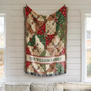 May include: A woven throw blanket featuring a patchwork pattern of red, green, and cream triangles decorated with snowflake and pine branch motifs. The blanket includes a horizontal band with the text THE WILLIAM FAMILY in dark green letters.