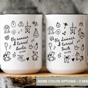 May include: Two white ceramic mugs with black handles and rims. The left mug features black line art of baby items and the text 'the summer I turned Auntie EST. 2026'. The right mug features similar icons and the text 'the Summer I turned Uncle EST. 2026'.