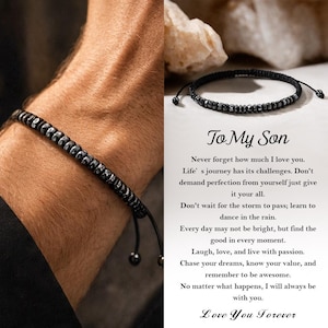 Puede incluir: Pulsera de cuentas negras con cordón ajustable. La pulsera presenta cuentas oscuras y metálicas ensartadas en un cordón negro. La imagen también incluye una tarjeta con el texto "To My Son" y un mensaje de amor.