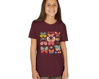 Peut inclure: Un t-shirt bordeaux orné d'un motif coloré de papillons et de fleurs. Le graphisme comprend diverses illustrations de papillons dans des tons de rose, jaune, bleu et vert, ainsi que de petites fleurs. Le t-shirt est porté par une personne.