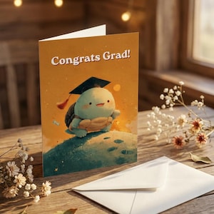 May include: A graduation greeting card with the text "Congrats Grad!" features a cartoon turtle wearing a graduation cap. The card is set on a wooden surface with a white envelope and decorative flowers.