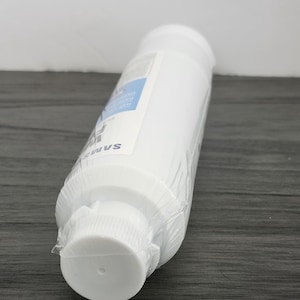 May include: A white cylindrical water filter, sealed in clear plastic. The filter has a white cap on one end and a label with blue text. The brand name "SAMSUNG" is visible on the side.