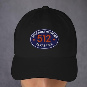 Può includere: Cappellino da baseball nero con visiera curva. Il cappellino presenta una toppa ricamata con la scritta "KEEP AUSTIN WEIRD" sopra "512 TEXAS USA" in un design circolare con colori blu, arancione e bianco.