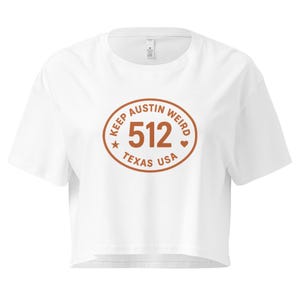 May include: White crop top with a round, brown graphic that reads "KEEP AUSTIN WEIRD 512 TEXAS USA". The shirt has short sleeves and a crew neck.