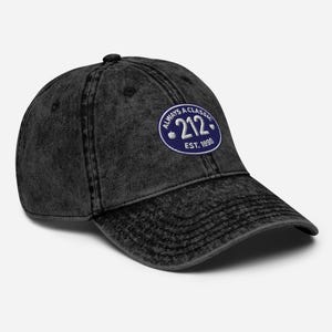 Puede incluir: Gorra de béisbol negra desgastada con visera curva. Cuenta con un parche circular con el texto "ALWAYS A CLASSIC 212 EST. 1898" en blanco y azul. La gorra tiene un aspecto vintage y desgastado.