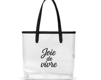 May include: Clear tote bag with black handles and trim. The bag features the phrase "Joie de vivre" in black script. The bag is designed to be transparent, allowing visibility of the contents.