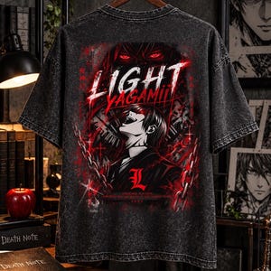 May include: A charcoal acid-wash t-shirt featuring a graphic print of Light Yagami from Death Note. The design includes red accents, chains, the text LIGHT YAGAMI, and Japanese characters. The character is shown with a laughing expression.