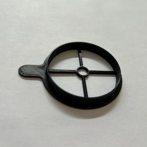 May include: Black plastic circle with a cross-shaped design in the center. The circle has a small handle on the side.