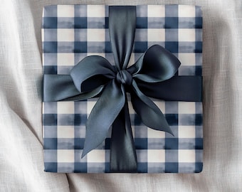 May include: A wrapped gift with blue and white checkered paper and a dark blue satin ribbon tied in a bow. The gift is presented on a light gray, textured surface.