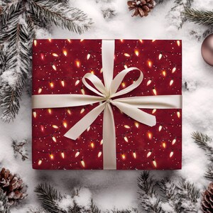 May include: A wrapped gift with a festive red background adorned with a pattern of glowing string lights and white dots. The gift is tied with a cream-colored ribbon and bow. The scene is set on a snowy surface with pine needles, pine cones, and a Christmas ornament.