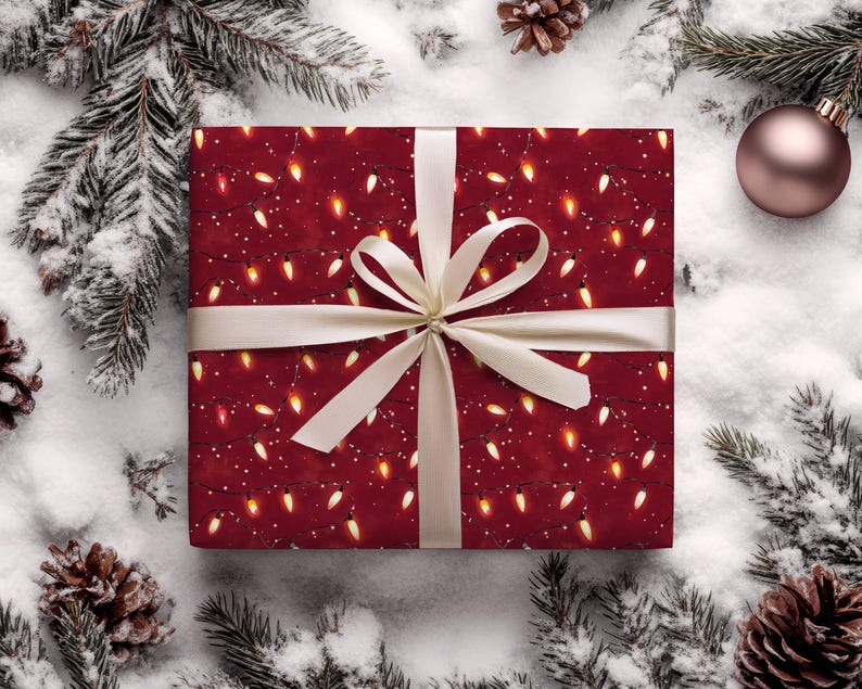 May include: A wrapped gift with a festive red background adorned with a pattern of glowing string lights and white dots. The gift is tied with a cream-colored ribbon and bow. The scene is set on a snowy surface with pine needles, pine cones, and a Christmas ornament.