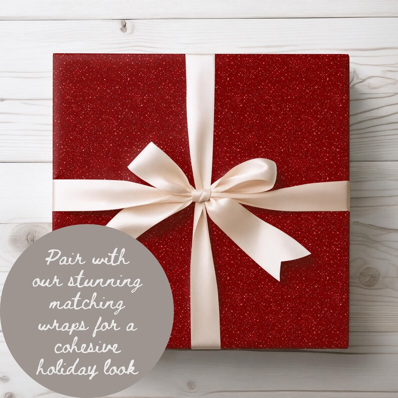 May include: A wrapped gift box with a red glitter finish, tied with a cream-colored satin ribbon and bow. The gift box is square-shaped and sits on a light wood-grain surface. The text on the image says, "Pair with our stunning matching wraps for a cohesive holiday look."