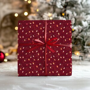 May include: A wrapped gift box with a festive design. The wrapping paper is a deep red color and covered in a pattern of white and yellow Christmas lights. A red ribbon is tied around the box in a bow.