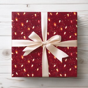 May include: A wrapped gift with a festive design. The wrapping paper is a deep red color, patterned with strings of Christmas lights in yellow and orange. A cream-colored satin ribbon is tied in a bow around the package.