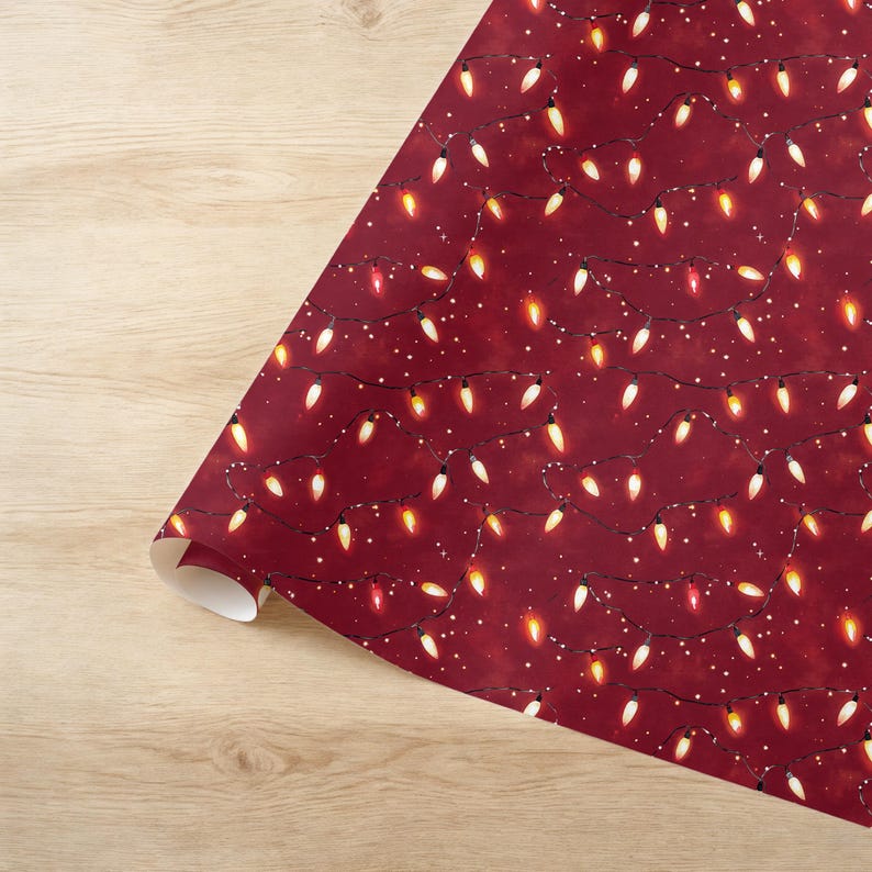 May include: A roll of wrapping paper with a festive design. The paper features a deep red background adorned with strings of Christmas lights in various colors, including white, yellow, and red. Small white dots add to the holiday theme.