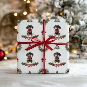 May include: A wrapped gift with white paper featuring a repeating pattern of dachshunds wearing red bows, Christmas trees, and festive greenery. The gift is tied with a red satin ribbon and bow, perfect for the holiday season.