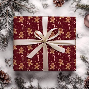 May include: A wrapped gift with a festive gingerbread man and candy cane pattern on a burgundy background. The gift is tied with a cream-colored ribbon and bow. The background features pine needles, pine cones, and a Christmas ornament.