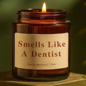 Peut inclure: Une bougie allumée dans un pot en verre brun avec une étiquette qui dit "Smells Like A Dentist". La bougie est posée sur une surface verte avec un fond vert foncé. La bougie est de 255 grammes.