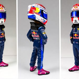 Könnte beinhalten: Eine Sammlerfigur eines Rennfahrers in einem dunkelblauen Rennanzug mit Sponsorenlogos wie Oracle und Red Bull. Die Figur trägt einen weiß-rot-blauen Helm mit blauem Visier und leuchtend pinkfarbene Rennstiefel an den Füßen.