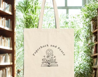 May include: Cream-colored tote bag with the words "paperback and peace" in a curved font. The bag features a graphic of an open book with flowers and a peace symbol. The bag has a handle for carrying.