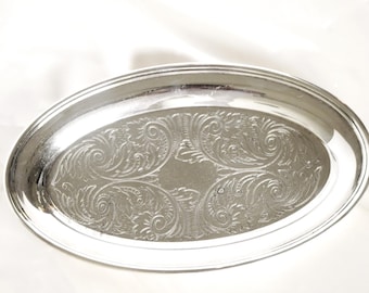 Könnte beinhalten: Eine ovale silberne Servierplatte mit einem gravierten floralen Muster. Die Platte hat einen erhöhten Rand und eine polierte Oberfläche. Die dekorative Platte eignet sich zum Servieren oder Ausstellen.