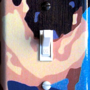 May include: A light switch cover with a cartoon pug dog design. The dog is brown, black, and white with a blue background. The switch is white and says "ON".