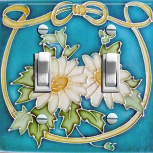May include: A light blue ceramic light switch cover with a white daisy floral design and a gold ribbon bow. The switch cover has two toggle switches with the word "ON" printed on them.