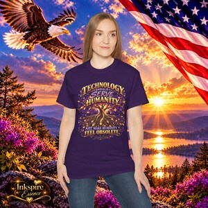 May include: A dark purple short-sleeve t-shirt featuring a graphic of a golden tree with roots and the text: TECHNOLOGY SHOULD SERVE HUMANITY NOT MAKE HUMANITY FEEL OBSOLETE. The design includes intricate golden leaf and root details.