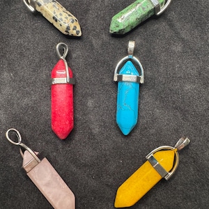 May include: Six gemstone pendant necklaces in various colors: speckled beige, green, red, turquoise, pink, and yellow. Each pendant is a hexagonal crystal shape with a silver-colored metal cap and loop for a chain.