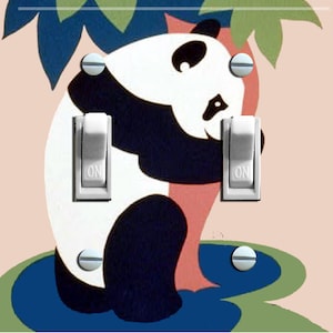 Op de afbeelding: Een lichtschakelaar-afdekplaat met een zwart-witte pandabeer die op een blauw en groen waterlelieblad zit. De panda houdt zich vast aan een roze boomstam. De schakelaar-afdekplaat heeft twee witte schakelaars met het woord "ON" erop.