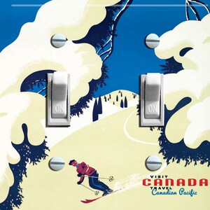 May include: A vintage-style light switch cover featuring a skier on a snowy mountain slope. The background is blue with white snow-covered trees. The text "VISIT CANADA TRAVEL Canadian Pacific" is at the bottom of the image.