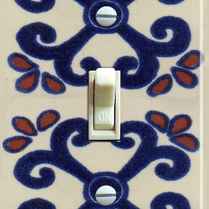 Pode incluir: Um interruptor de luz branco com a palavra "ON" impressa nele. O interruptor é cercado por uma placa de cerâmica decorativa com um padrão floral azul e vermelho.