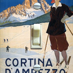 May include: A vintage travel poster for Cortina d'Ampezzo, Italy, featuring a woman in a red hat skiing down a snowy mountain slope. The poster is designed to look like a light switch with the word "ON" printed on the switch.