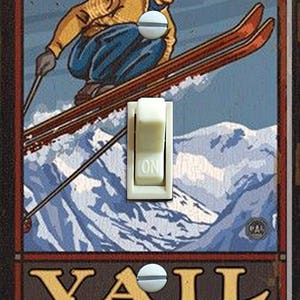 May include: A vintage-style light switch cover featuring a skier in a yellow sweater and blue trousers, skiing down a mountain with the text "VAIL COLORADO" at the bottom.