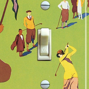 May include: A light switch plate with a vintage illustration of golfers on a green course. The plate features a white toggle switch with the word "ON" printed on it. The text "TRUCKEE" is printed in yellow at the bottom of the plate.