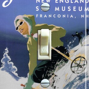 May include: A light switch cover featuring a vintage ski poster with the text "Ski Fun, New England Ski Museum, Franconia, NH". The poster shows a skier in a blue and white jacket and a green hat skiing down a snowy slope.