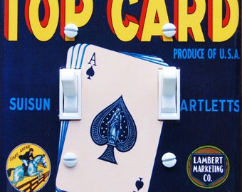 May include: A vintage-style light switch plate featuring a playing card with the Ace of Spades. The switch plate is blue with yellow, red, and white text that reads "Top Card Produce of U.S.A. Suisun Artletts Lambert Marketing Co. Main Office Sacramento, Calif."