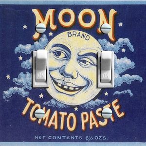 Könnte beinhalten: Eine Vintage-Lichtschalterplatte mit blauem Hintergrund, einem weißen Mondgesicht und dem Text "MOON BRAND TOMATO PASTE NET CONTENTS 6 1/2 OZ."