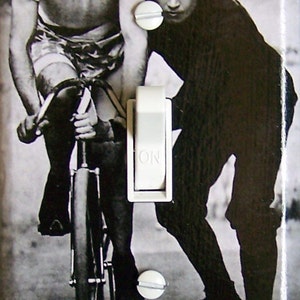 Puede incluir: Una fotografía en blanco y negro de dos hombres en una bicicleta. El hombre de delante lleva una gorra y un jersey. El hombre de detrás lleva una camisa blanca y sujeta el manillar. La bicicleta tiene una rueda delantera grande y una rueda trasera más pequeña.