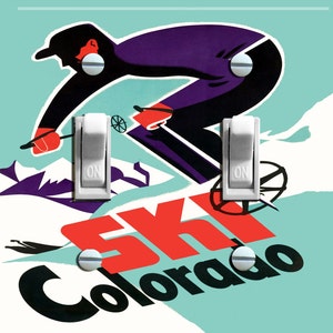 May include: A light blue and white light switch cover with a vintage illustration of a skier in a purple and black suit. The text "Ski Colorado" is in red and black letters.