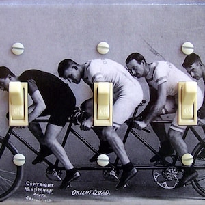 Könnte beinhalten: Ein Schwarzweißfoto von vier Männern, die ein Tandemfahrrad fahren. Die Männer tragen Vintage-Kleidung und das Fahrrad hat einen langen Rahmen mit zwei Sitzen. Das Bild ist auf einem hellgrauen Hintergrund mit vier hellbeigen Kippschaltern gedruckt.