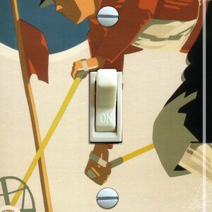May include: Light switch cover with a vintage ski poster design. The artwork shows a skier in orange clothing on a snowy slope, with the text "NEW HAMPSHIRE" at the bottom. The switch is in the "ON" position.