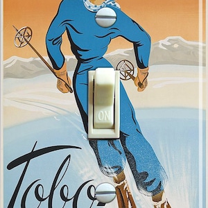 May include: A vintage poster advertising Tobo Skidan ski equipment. The poster features a woman in a blue ski suit and a white hat, skiing down a snowy mountain. The text on the poster reads "Tobo Skidan" and "A-B Tobo Skidfabrik, Tobo."